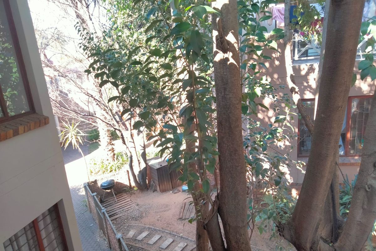 An elevated view of a rear garden area featuring mature trees, paved pathways, and brick building facades.