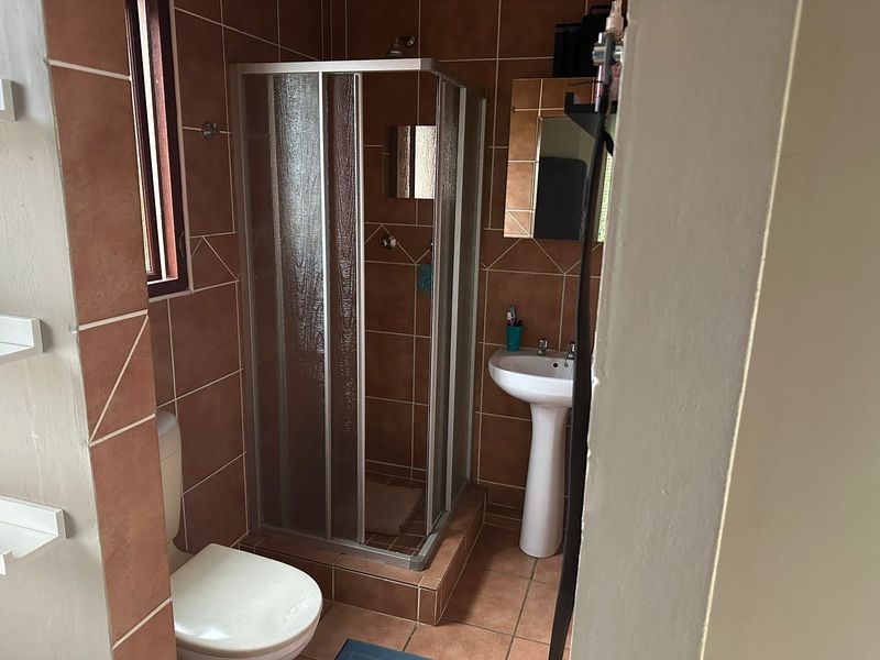 A functional bathroom featuring a shower enclosure, pedestal basin, and toilet, finished with terracotta-style wall and floor tiles.