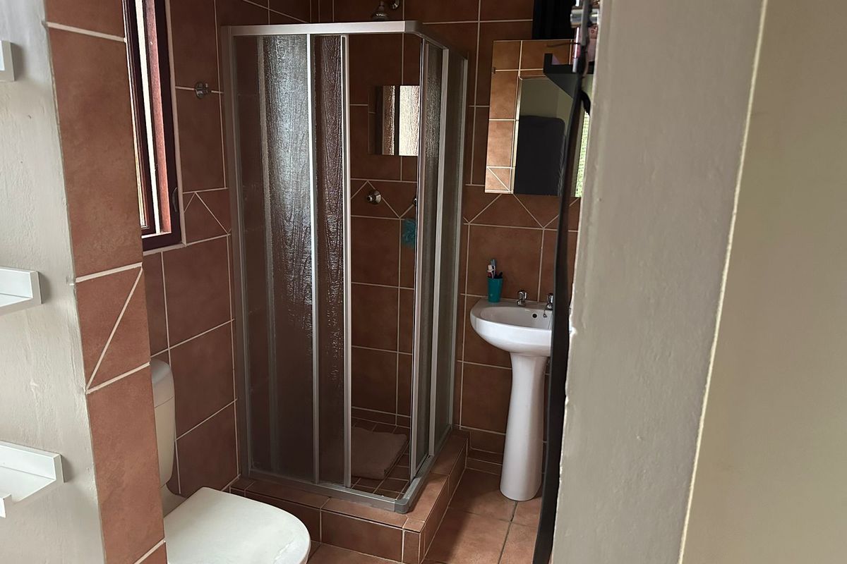 A functional bathroom featuring a shower enclosure, pedestal basin, and toilet, finished with terracotta-style wall and floor tiles.