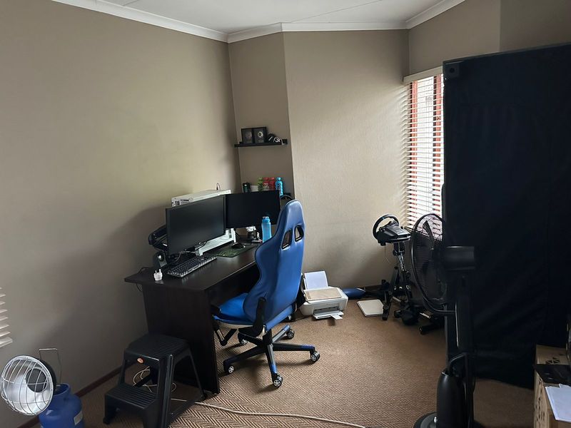 A functional home office space featuring neutral wall tones, carpeted flooring, and window blinds, providing a versatile area for work or study.