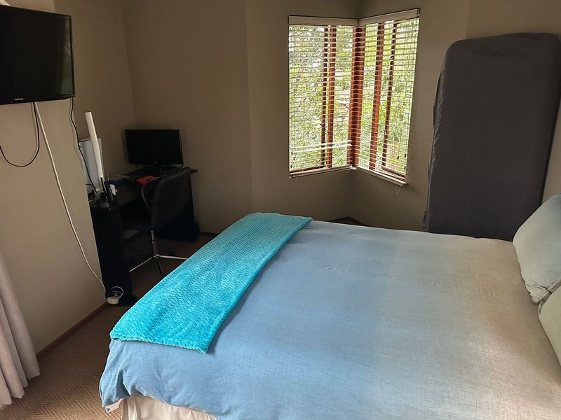 A bedroom featuring a bay window with venetian blinds and carpeted flooring, providing a functional space with natural light.