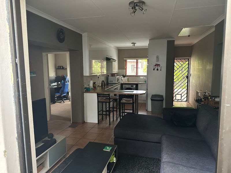 Open-plan living area featuring a kitchen with built-in cabinetry, a breakfast bar, and tiled flooring, leading to an adjacent room and exterior access.