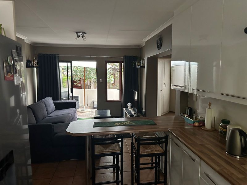 Open-plan living area featuring a modern kitchen with breakfast bar, tiled flooring, and direct access to an outdoor patio through sliding glass doors.