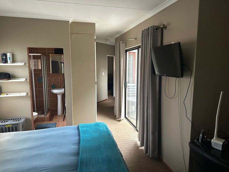 A bedroom featuring an en-suite bathroom with a shower and pedestal basin, plus a sliding glass door providing access to an outdoor area.