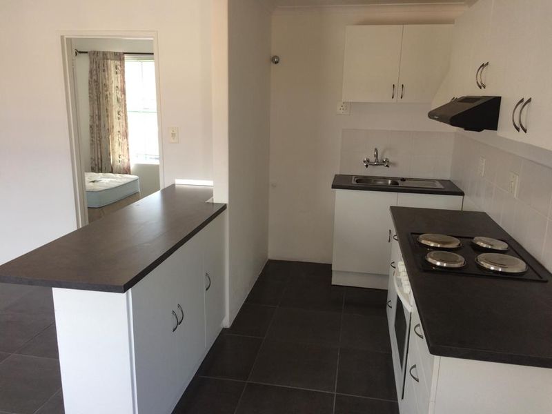 A functional kitchen featuring white cabinetry, dark laminate countertops, built-in oven and hob, and tiled flooring, with an open-plan layout.