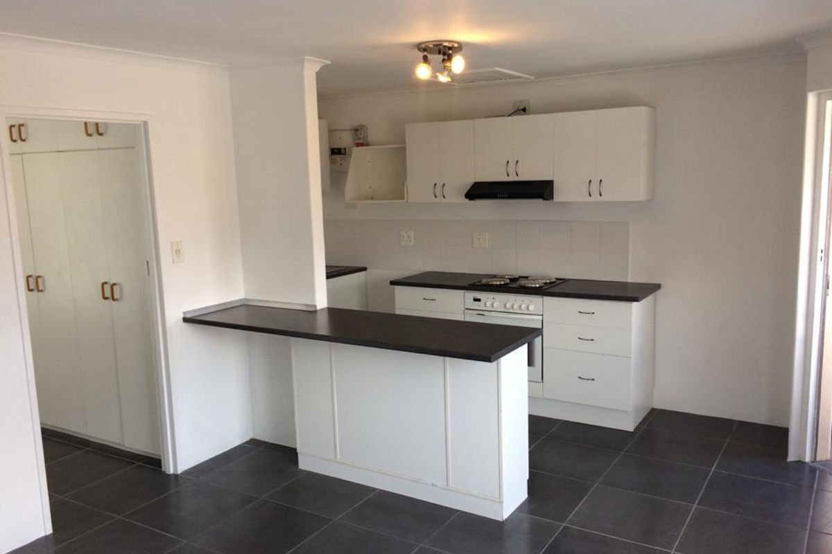 A clean, functional kitchen featuring white cabinetry, dark countertops, a built-in oven and hob, and a breakfast bar, set against dark floor tiles.