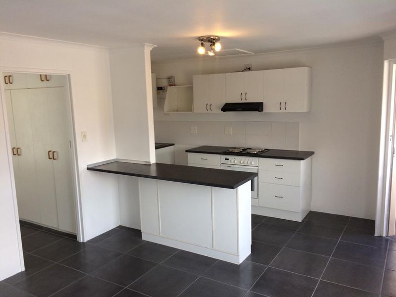 A clean, functional kitchen featuring white cabinetry, dark countertops, a built-in oven and hob, and a breakfast bar, set against dark floor tiles.