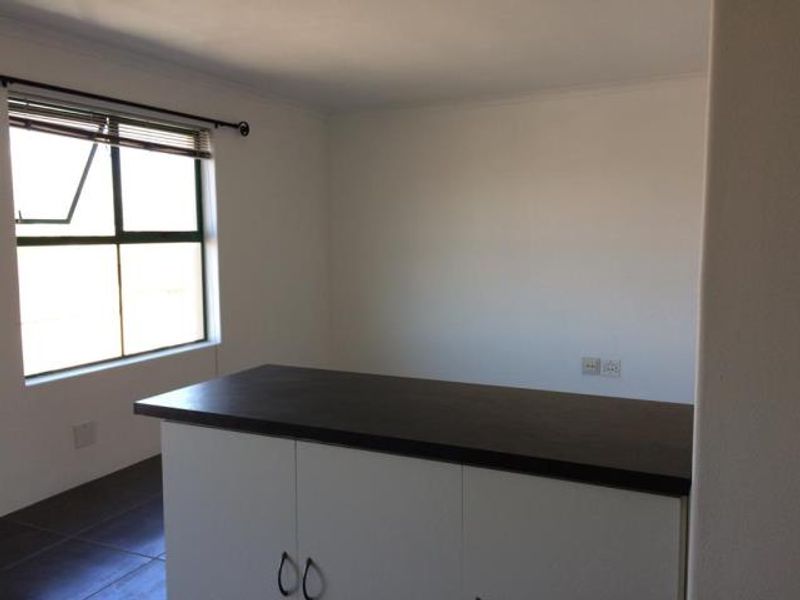 An empty open-plan living area featuring tiled flooring, built-in cabinetry with a dark countertop, and a large window providing natural light.