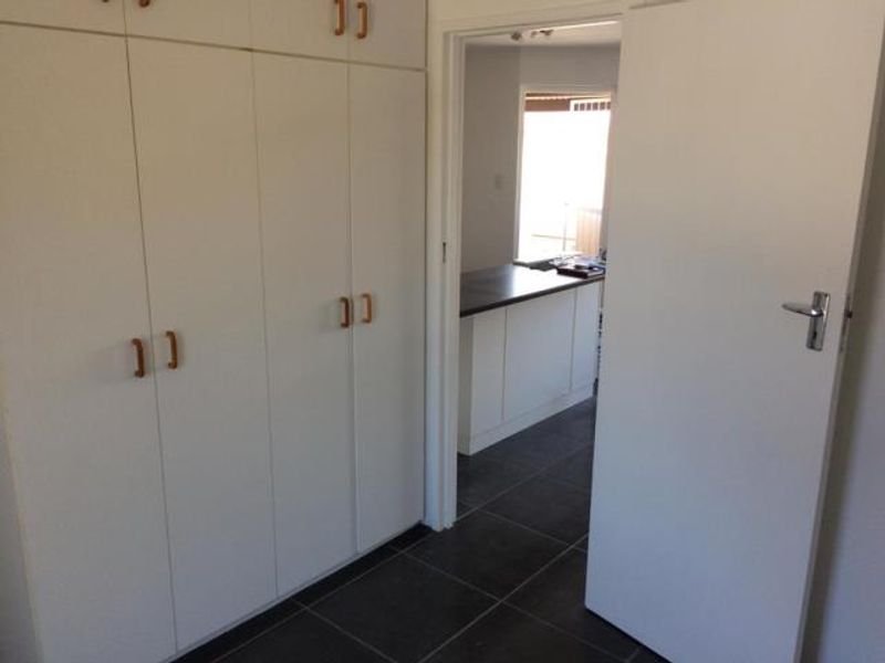 A hallway featuring extensive built-in storage cupboards and dark tiled flooring, leading through to an open-plan kitchen area.
