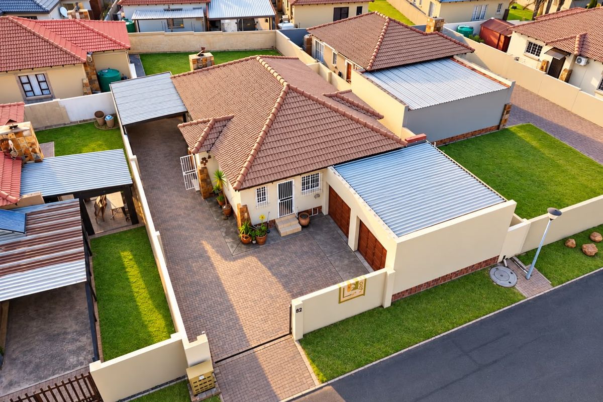 Aerial view of a residential property featuring a tiled roof, paved driveway, double garage, and a well-maintained garden with perimeter walling.