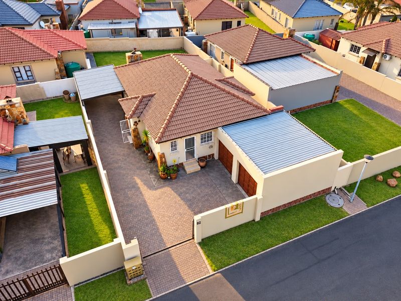 Aerial view of a residential property featuring a tiled roof, paved driveway, double garage, and a well-maintained garden with perimeter walling.