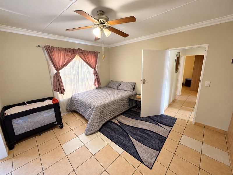 A functional bedroom featuring tiled flooring, a ceiling fan, and neutral wall finishes, offering a comfortable and well-maintained living space.