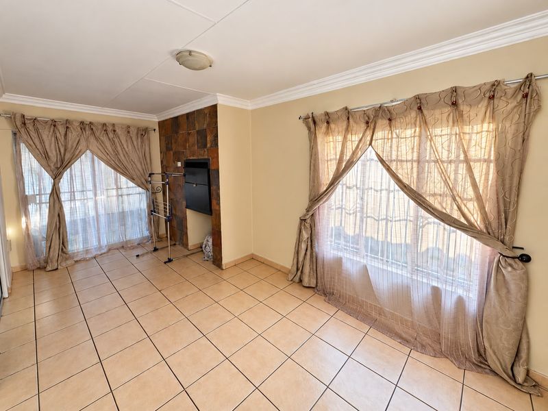 A spacious living room featuring tiled flooring, a built-in fireplace with stone cladding, and large windows with security bars.