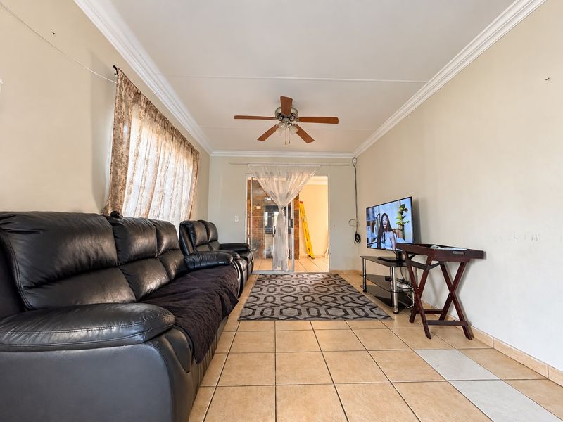 A living room featuring tiled flooring, a ceiling fan, and crown molding, providing a functional space with potential for cosmetic updates.