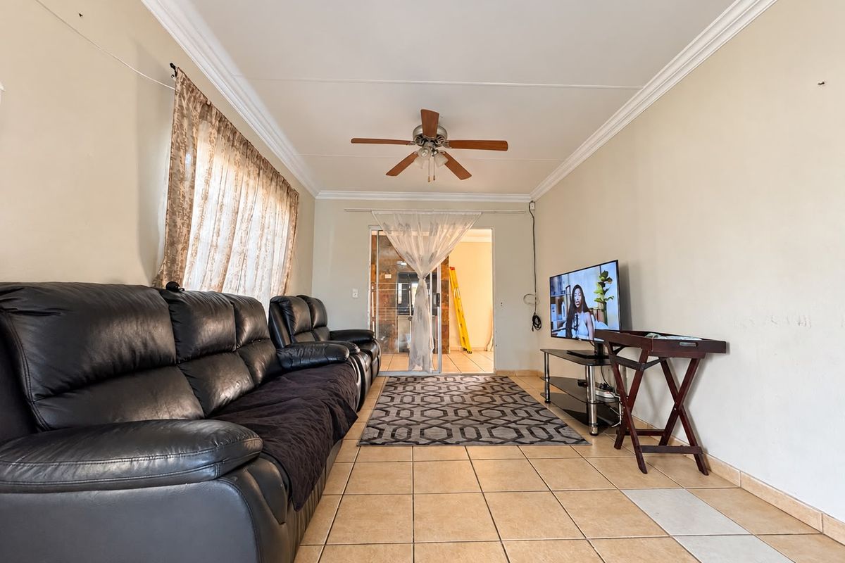 A living room featuring tiled flooring, a ceiling fan, and crown molding, providing a functional space with potential for cosmetic updates.