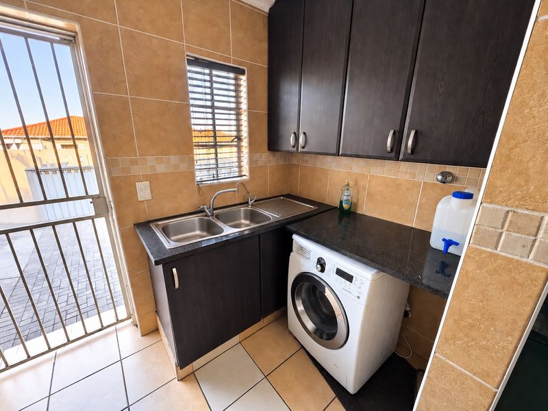 Functional laundry area featuring dark cabinetry, granite countertops, a double basin sink, and tiled finishes with direct access to the exterior.