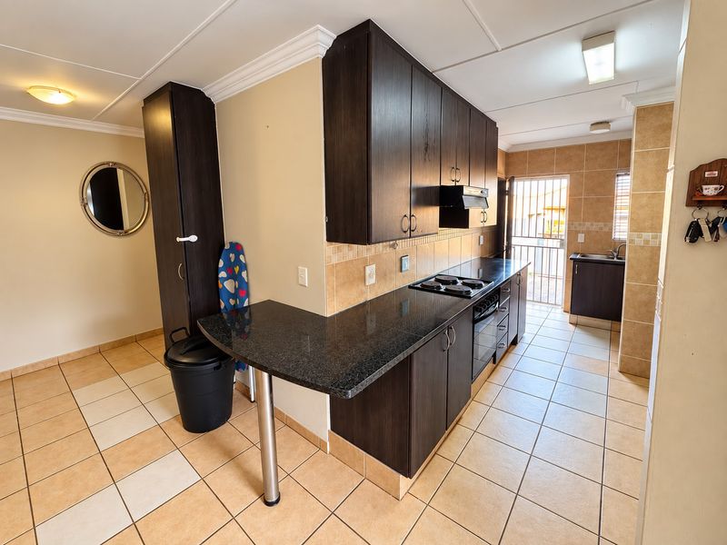 Functional kitchen featuring dark wood cabinetry, granite countertops, built-in oven, electric hob, and tiled flooring with direct access to an exterior security gate.