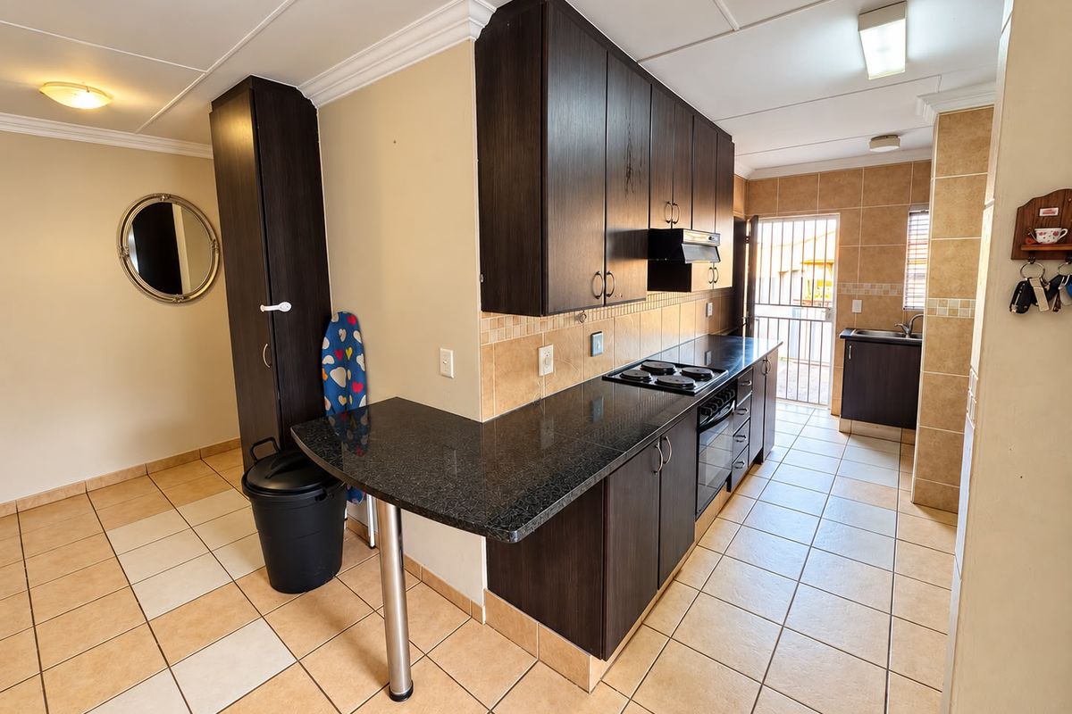 Functional kitchen featuring dark wood cabinetry, granite countertops, built-in oven, electric hob, and tiled flooring with direct access to an exterior security gate.