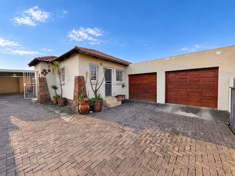 Front elevation of a house featuring a paved driveway, double garage with wooden doors, and a tiled roof entrance with security features.