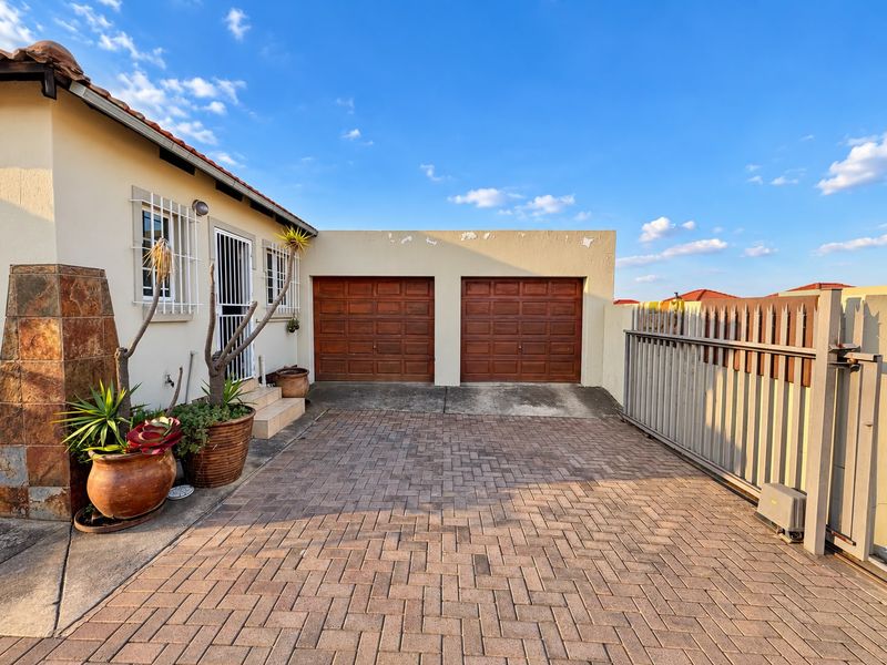 Front exterior view featuring a double garage with wooden doors, paved driveway, and secure gated entrance with stone cladding accents.
