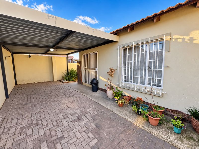 A paved driveway featuring a covered carport, security bars on windows and doors, and a tiled roof structure.