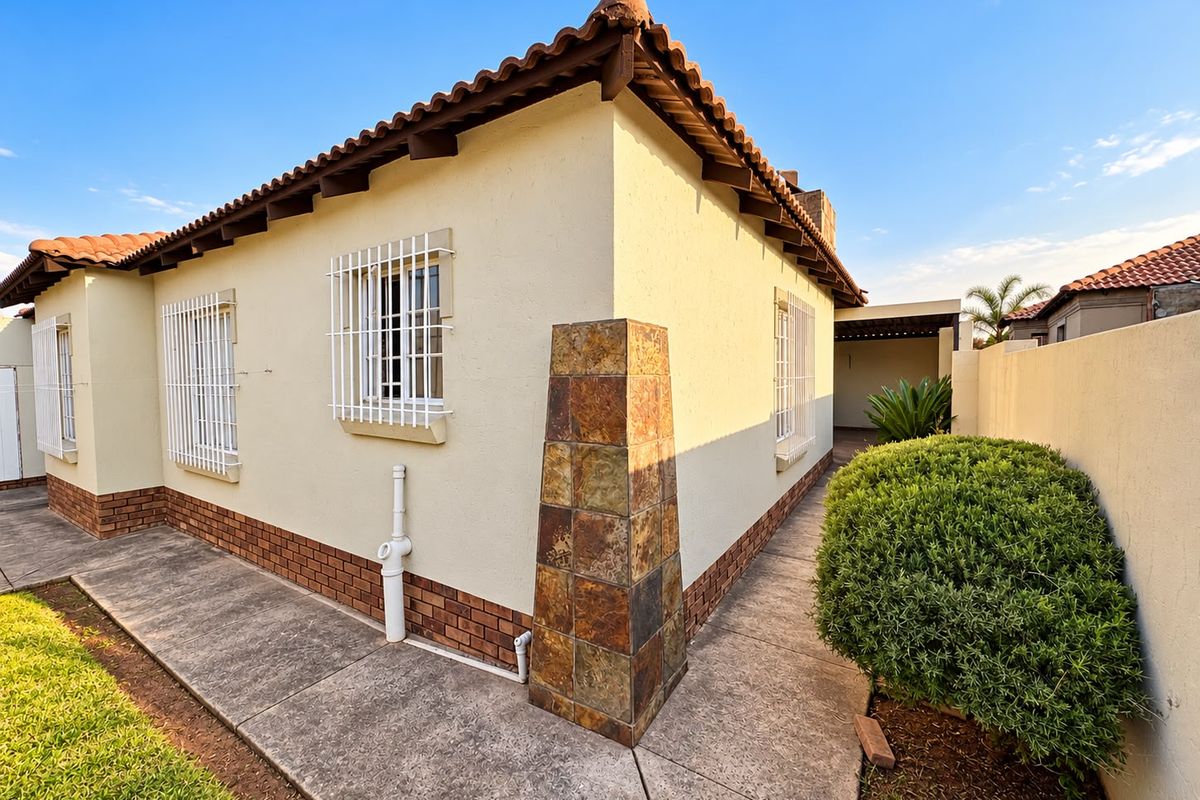 Rear exterior view of the house featuring a stone-clad pillar, terracotta roof tiles, security bars on windows, and a paved walkway along the boundary wall.