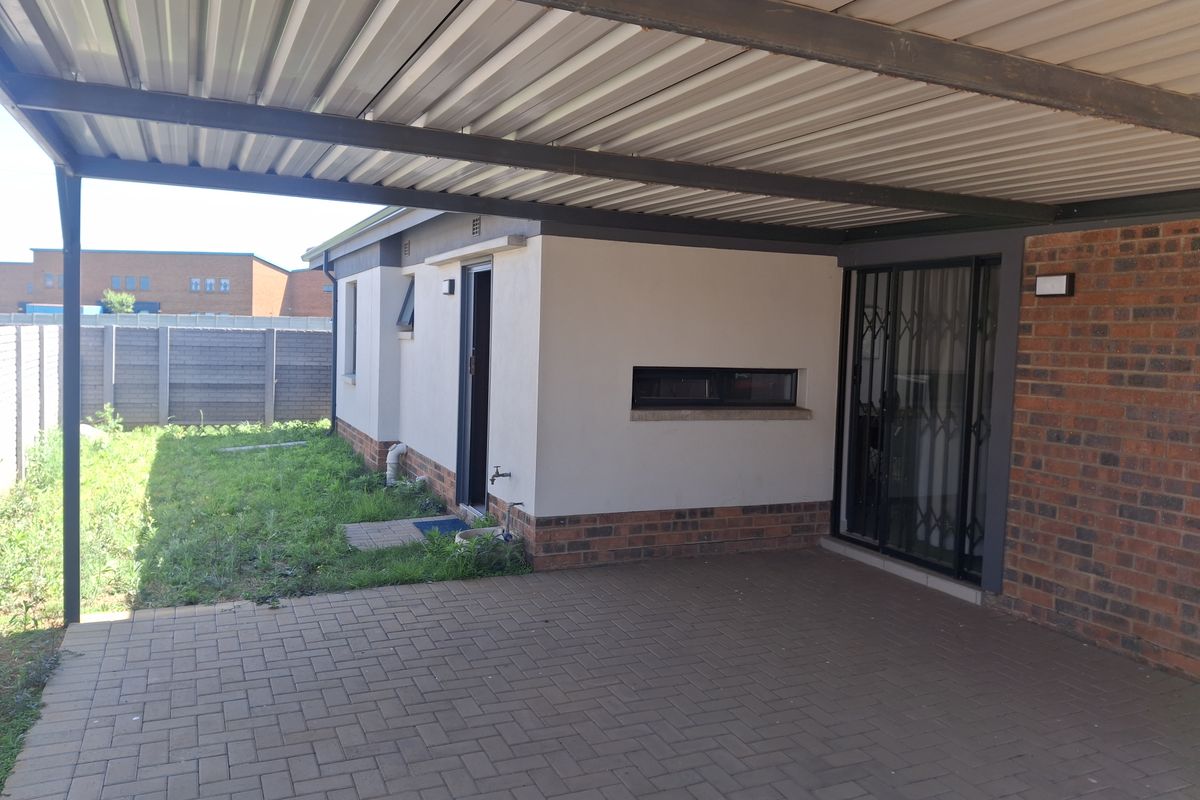 Rear exterior view featuring a covered carport, paved driveway, and access to the garden area with boundary walling.