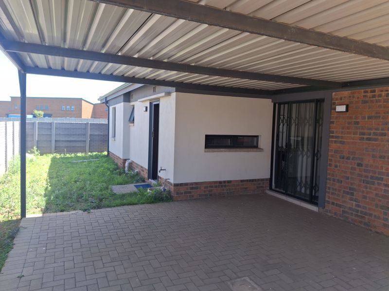 Rear exterior view featuring a covered carport, paved driveway, and access to the garden area with boundary walling.