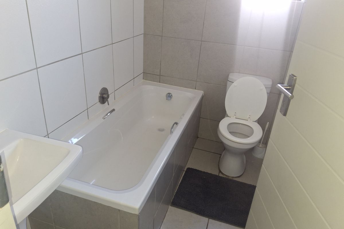 A functional bathroom featuring a bathtub, toilet, and wall-mounted basin with neutral tiled finishes.