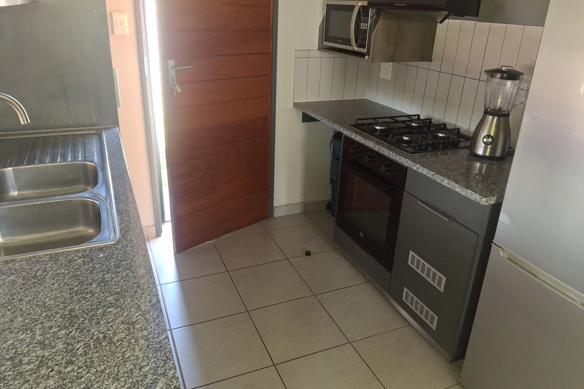 Compact kitchen featuring granite countertops, built-in oven, gas hob, extractor fan, and tiled flooring with direct access to an exterior door.