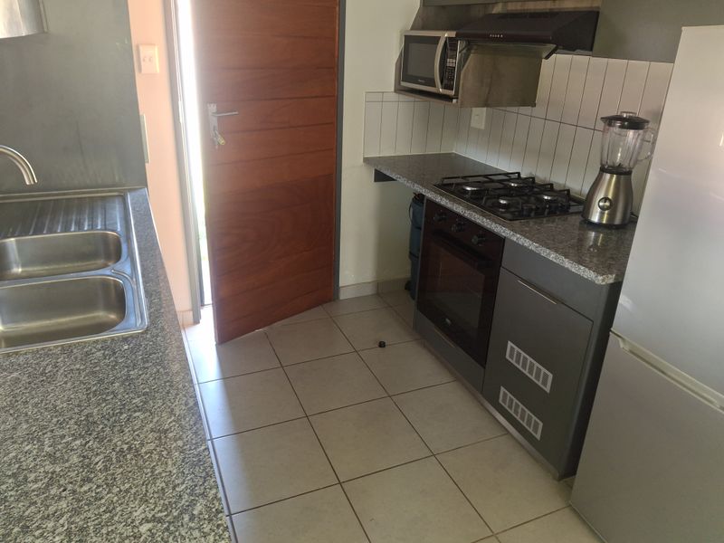 Compact kitchen featuring granite countertops, built-in oven, gas hob, extractor fan, and tiled flooring with direct access to an exterior door.