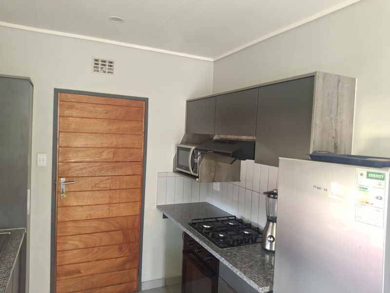 A functional kitchen featuring modern grey cabinetry, granite countertops, a gas hob, built-in oven, and integrated microwave with a tiled backsplash.
