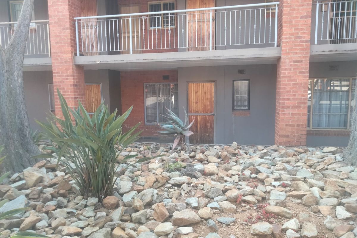 Rear view of a multi-story flat complex featuring brick pillars, metal balcony railings, and a low-maintenance rock garden.