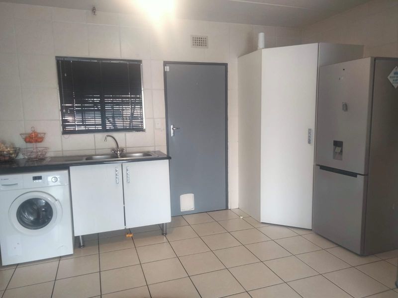A functional laundry area featuring tiled flooring, wall-mounted cabinetry, a stainless steel sink, and space for integrated appliances.