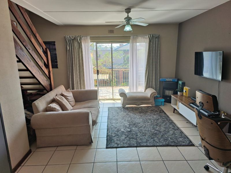 Spacious living room featuring tiled flooring, a ceiling fan, and a wooden staircase, with direct access to a balcony through sliding glass doors.