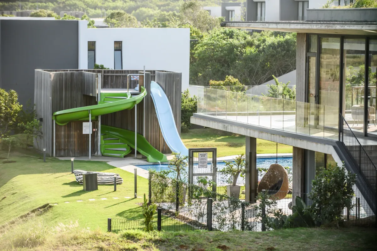 A well-maintained outdoor pool area featuring a water slide, modern timber structure, and a spacious balcony overlooking the landscaped garden.