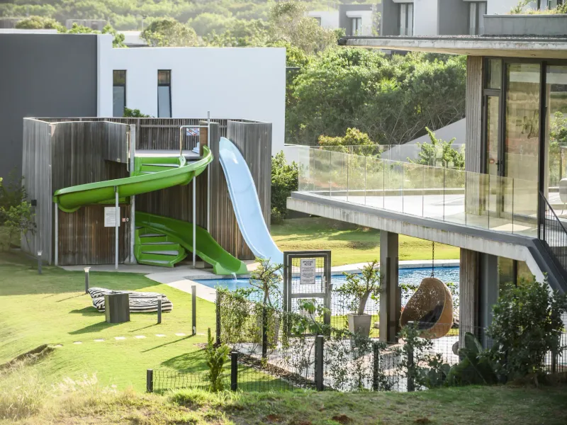 A well-maintained outdoor pool area featuring a water slide, modern timber structure, and a spacious balcony overlooking the landscaped garden.
