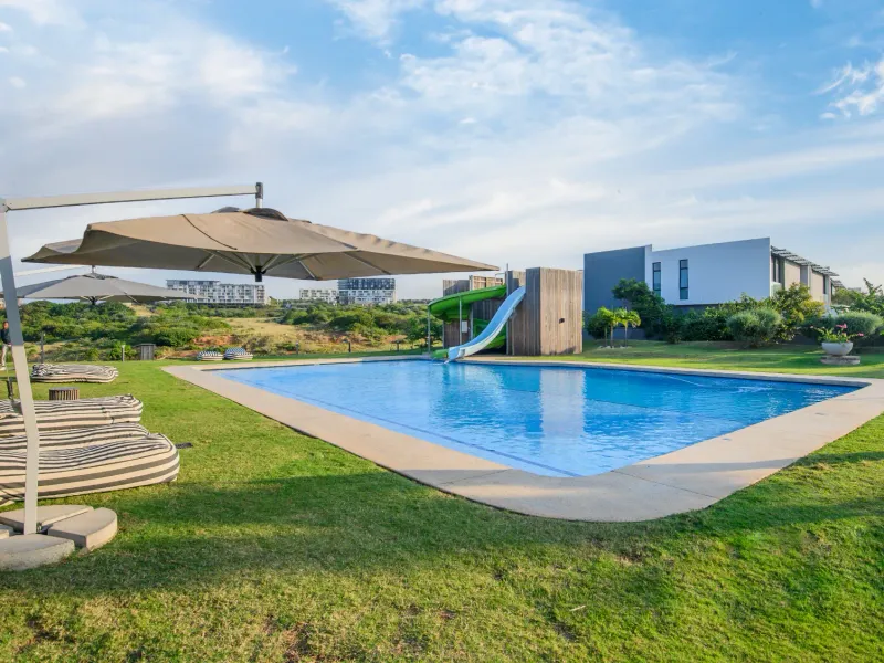 A well-maintained outdoor swimming pool area featuring a built-in slide, surrounded by landscaped lawn and open views.