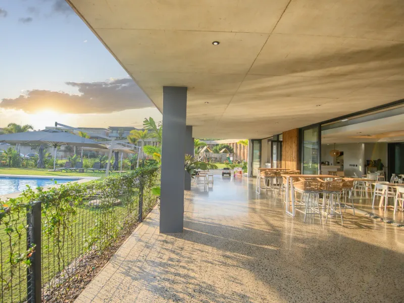 Spacious covered patio featuring polished concrete floors and recessed lighting, seamlessly connecting to the outdoor swimming pool area through large sliding glass doors.