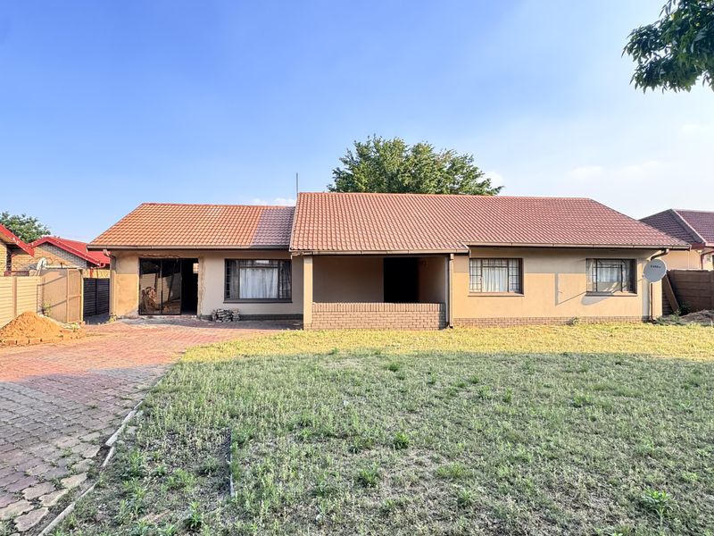 Front view of a single-story residential house featuring a tiled roof, paved driveway, and a large front lawn area.