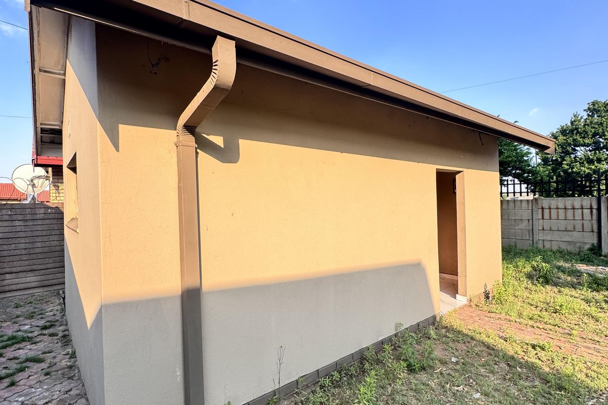 Rear view of the property showing the exterior wall, guttering system, and surrounding yard area.
