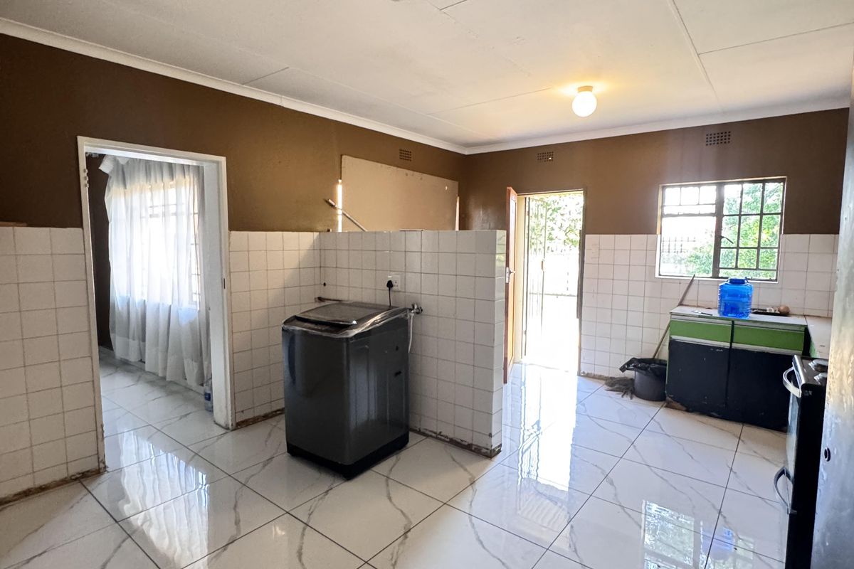 A spacious kitchen area featuring modern marble-look floor tiles, a central partition wall, and basic utility connections, currently awaiting final finishes and cabinetry installation.