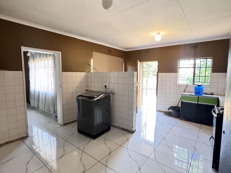 A spacious kitchen area featuring modern marble-look floor tiles, a central partition wall, and basic utility connections, currently awaiting final finishes and cabinetry installation.