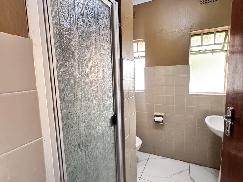 A functional bathroom featuring a shower enclosure, pedestal basin, toilet, and tiled finishes, currently requiring cosmetic updates to the wall surfaces.
