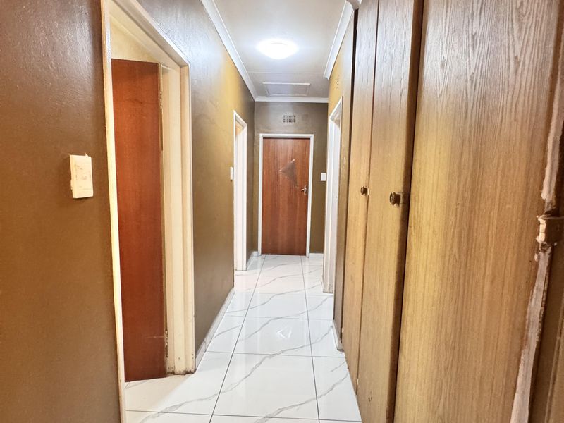 A functional hallway featuring white marble-look floor tiles, built-in wooden cupboards, and access to multiple rooms.