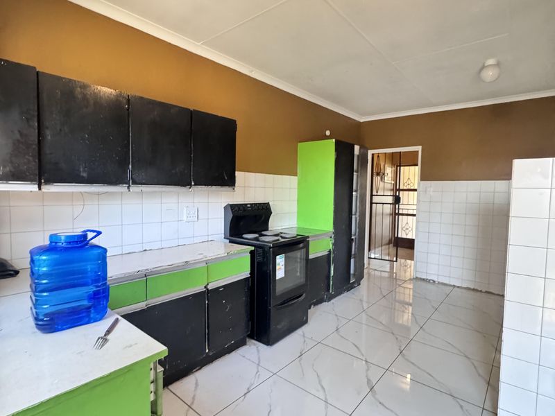 A functional kitchen featuring tiled flooring, a tiled backsplash, and built-in cabinetry with a freestanding oven, offering potential for cosmetic updates.