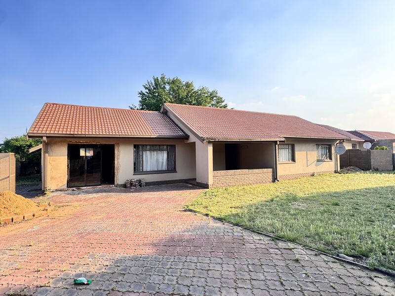 Front view of a single-story house featuring a tiled roof, paved driveway, and an unfinished exterior wall section near the entrance.