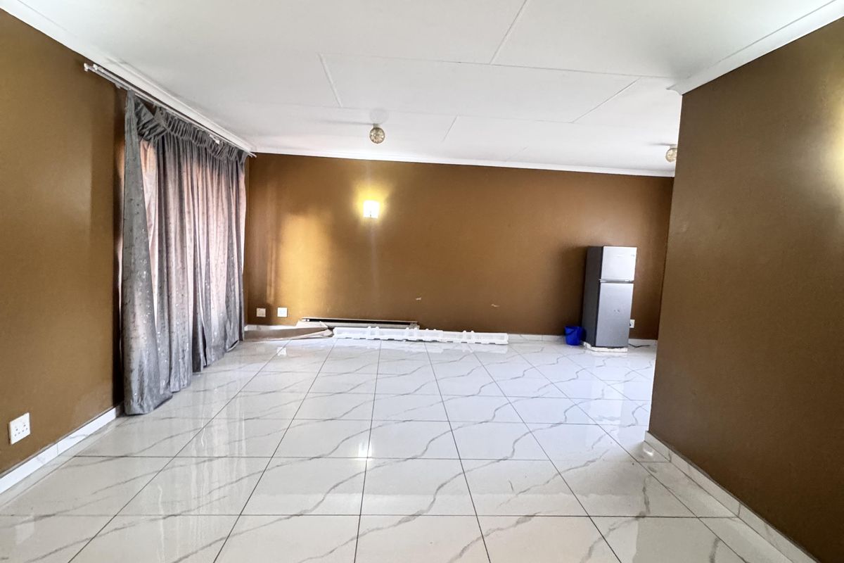 Spacious living area featuring polished marble-look floor tiles and neutral brown walls, offering a blank canvas for interior design and furniture placement.