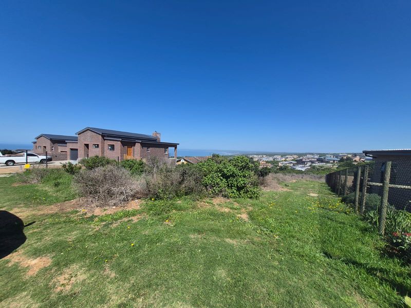A wide-angle view of a residential plot featuring a manicured lawn, perimeter fencing, and distant coastal scenery.