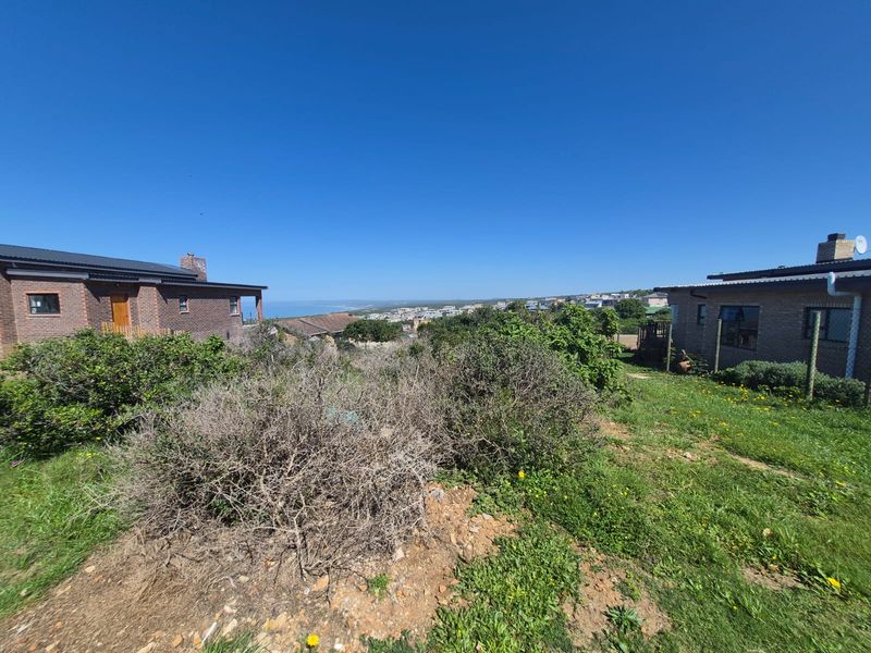 A wide-angle view overlooking a coastal residential area, captured from a vacant plot of land with surrounding established homes.